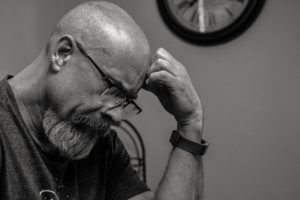 A grayscale picture of a man in deep thought with a hand on his forehead.