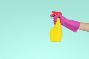 Hand with a pink glove on it holding a yellow spray bottle