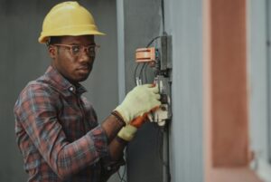 An electrician wearing a yellow safety helmet and checking an electrical panel.