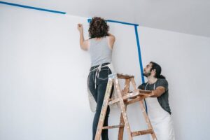 A man standing near the woman on the ladder, ready to paint the wall in a Seattle home remodel