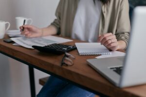 Woman sitting at a desk with a pen, a piece of paper, and a calculator.